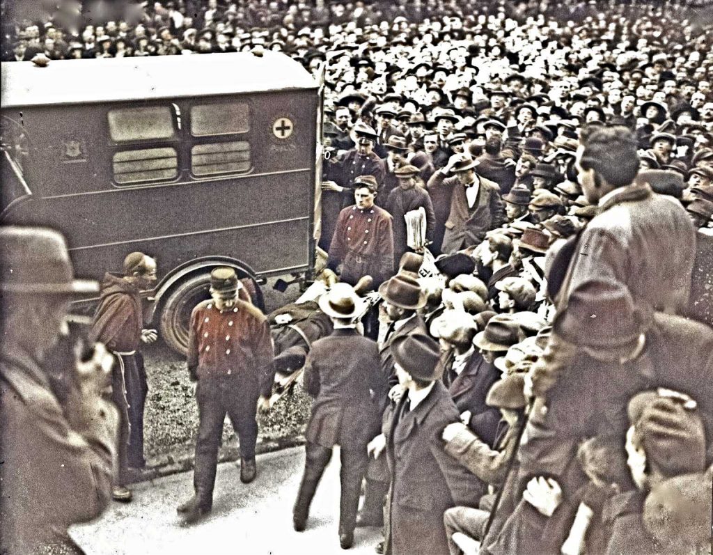 Enormous crowds celebrated the release of the hunger strikers from the Mountjoy Jail on Wednesday 14 April 1920. They were removed by ambulance to hospital. Slightly colourised newspaper picture, showing the ambulance with a huge crowd around it. Two ambulance staff carry a stretcher with a hunger striker on it.